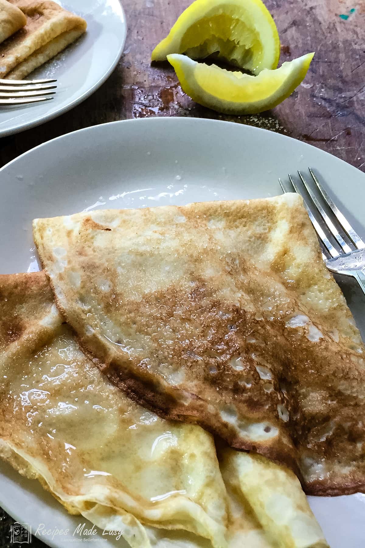 two English pancakes on a plate with squeeze lemon wedges behind.