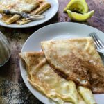 two plates of pancakes with lemon and sugar.