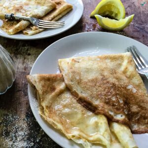 two plates of pancakes with lemon and sugar.