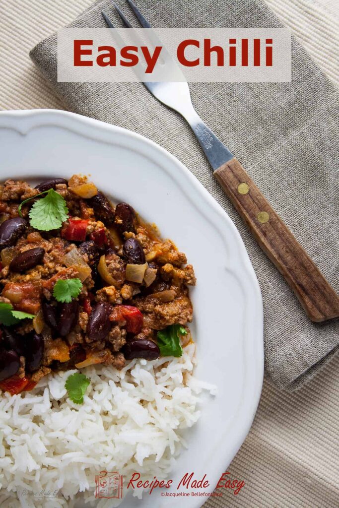 Easy chilli served with rice on white plate with fork and napkin on the side.