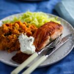 Pan-fried salmon and sweet potato chilli mash on a plate with fish knife and fork.