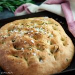 easy focaccia on a tray with oven cloth wrapped around back of tray.