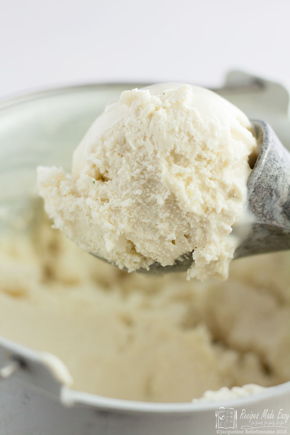 basil ice-cream in an ice cream scoop over a container of the ice cream.