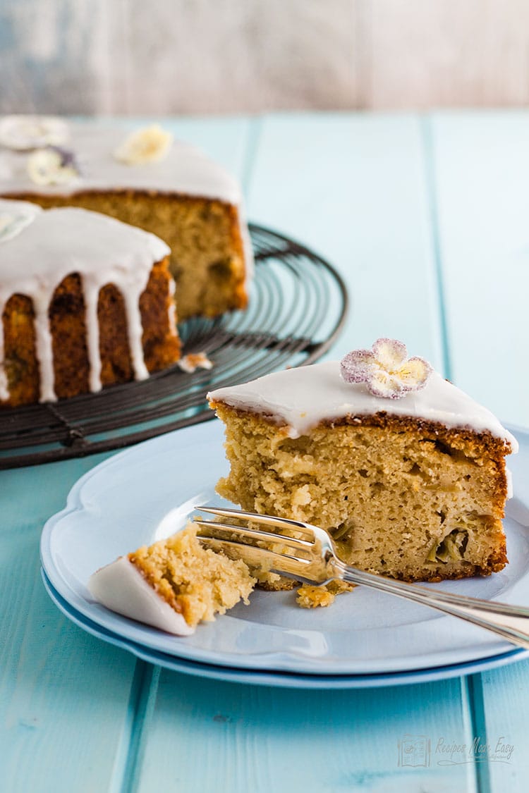 slice of rhubarb cake with elderflower drizzle icing on plate with piece broken with fork