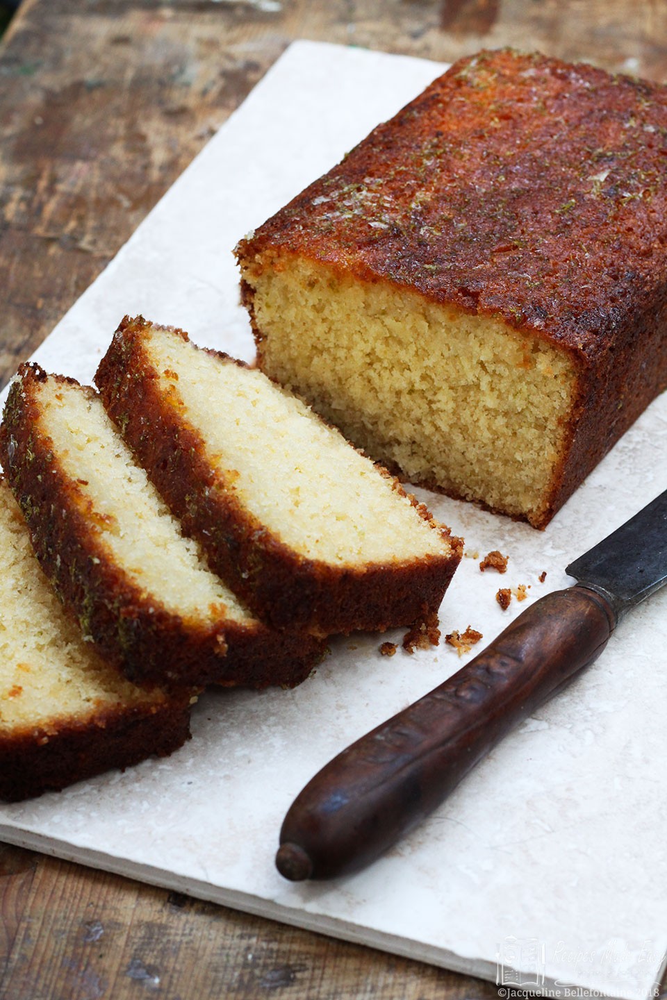 Coconut and lime drizzle cake with several slices and a knife on the board.