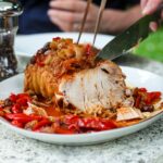 Slow-cooed weet and sour pork on serving plater being carved into slices.