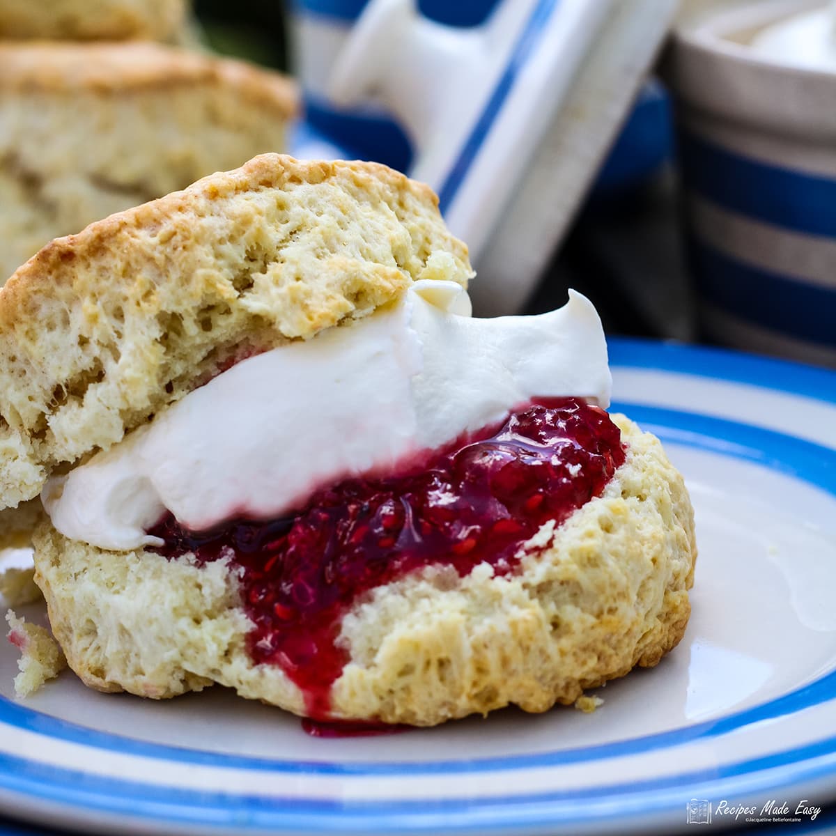 Scone split and filled with jam and cream on blue and white plate.