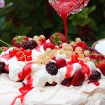 berry coulis being poured over the summer berry pavlova