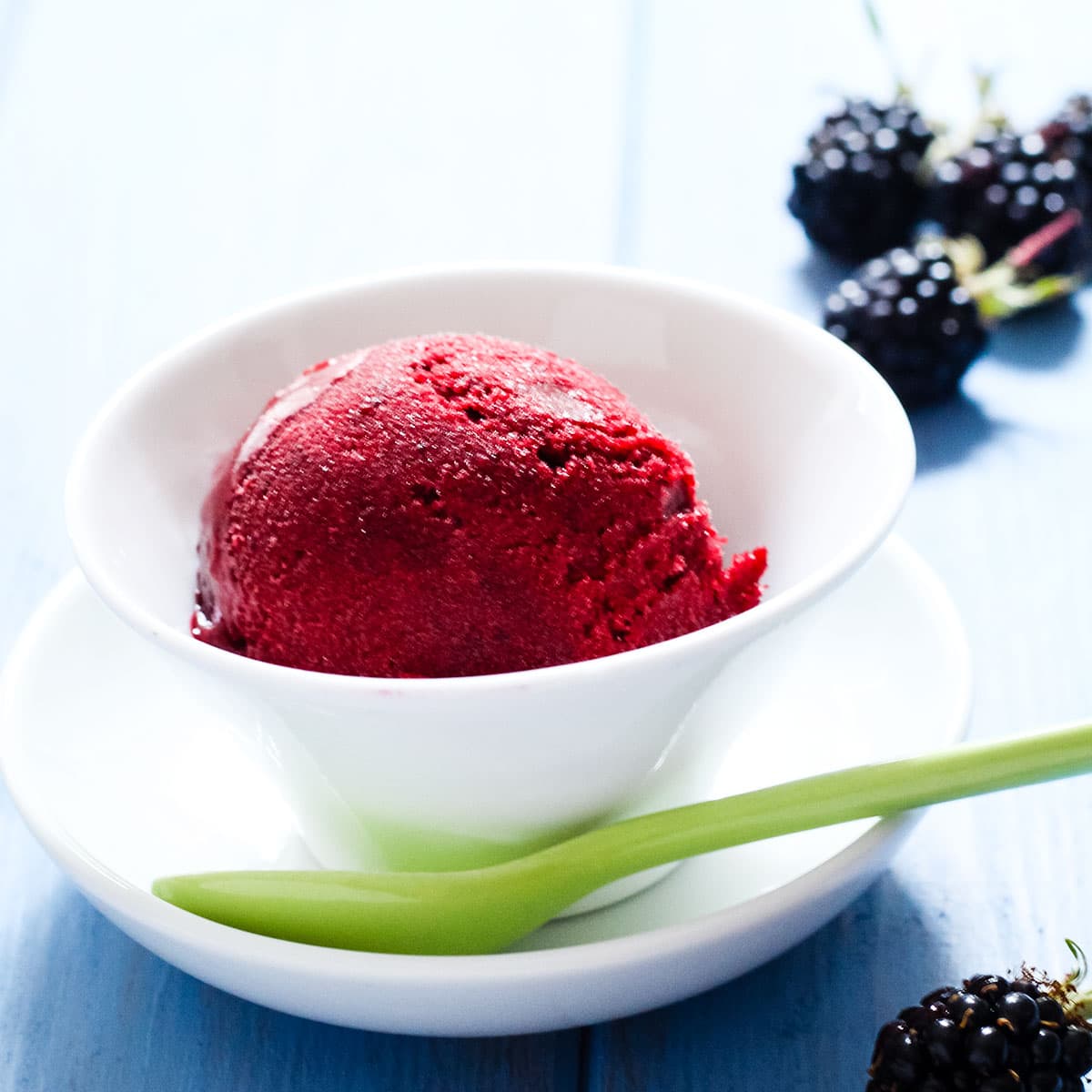 scoop of blackberry sorbet in a bowl with spoon on saucer.