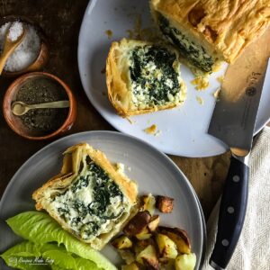 Two plates one with with spinach, ricotta and feta pie and a slice laying down the other with a slice served with lettuce and potatoes