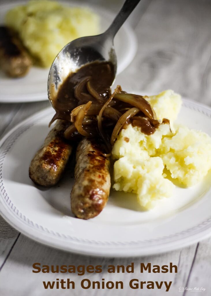 spooning gravy over sausages and mash in a plate.