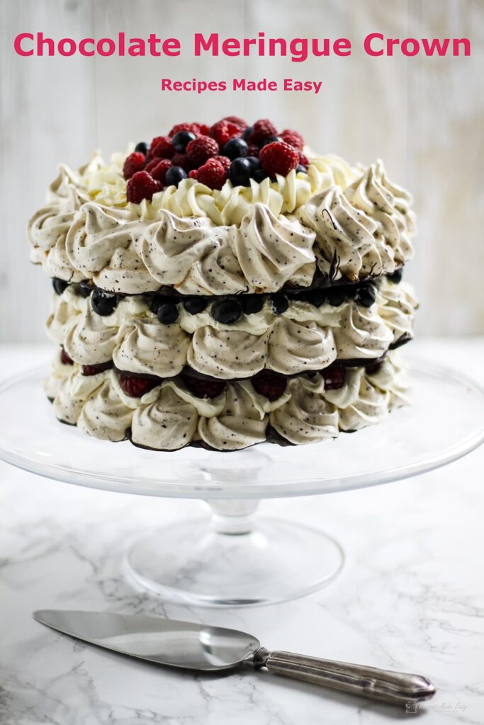 chocolate meringue crown on glass cake stand with cake slice in front.