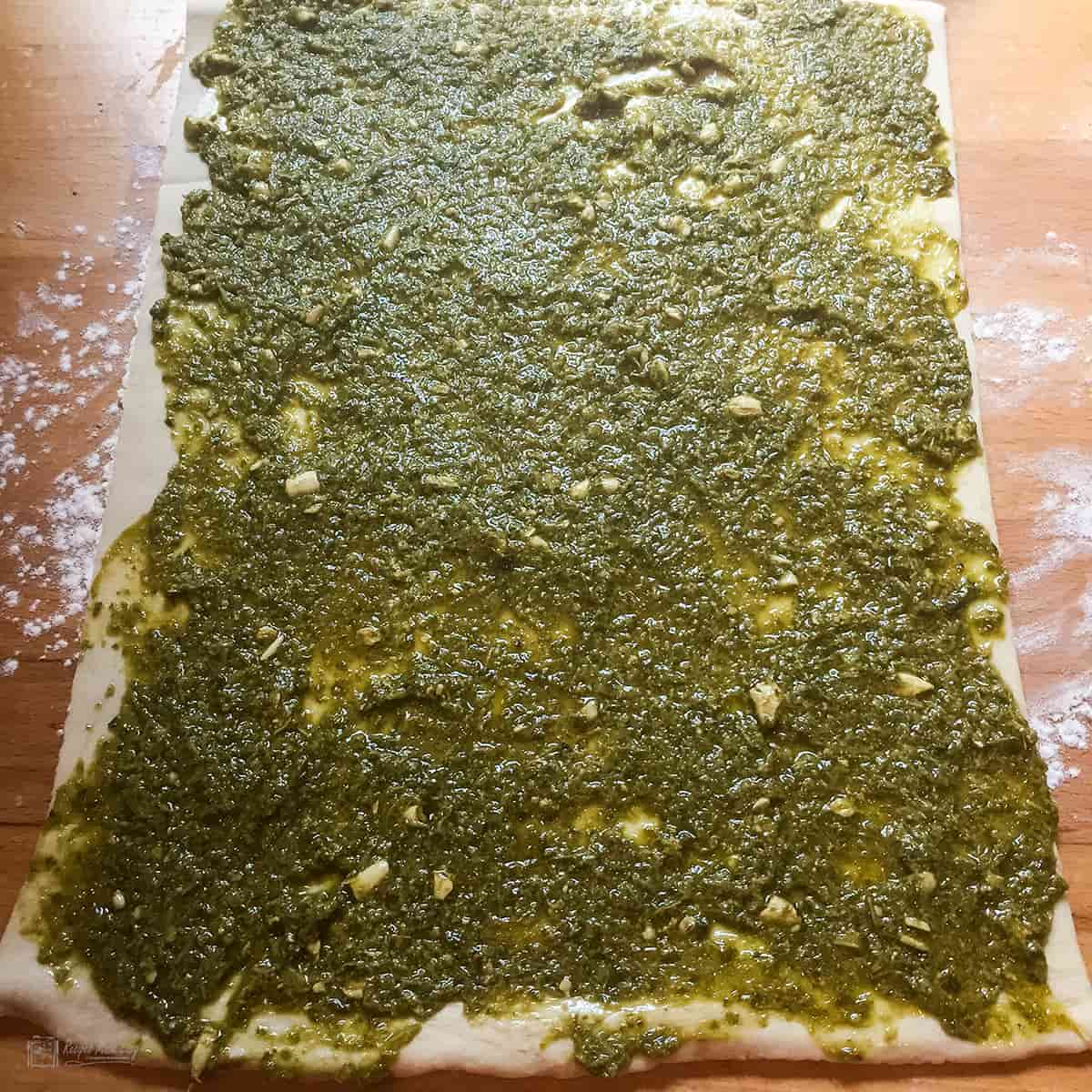 Pesto spread out to cover puff pastry sheet.