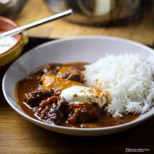 serving of easy beef goulash with rice. Garnished with soured cream and a sprinkling of paprika.