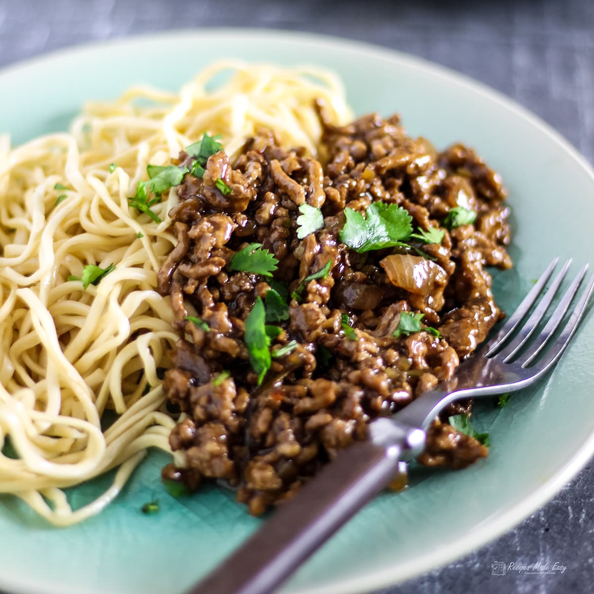 asian inspired spicy pork mince served with noodles on a green plate with fork on the side.