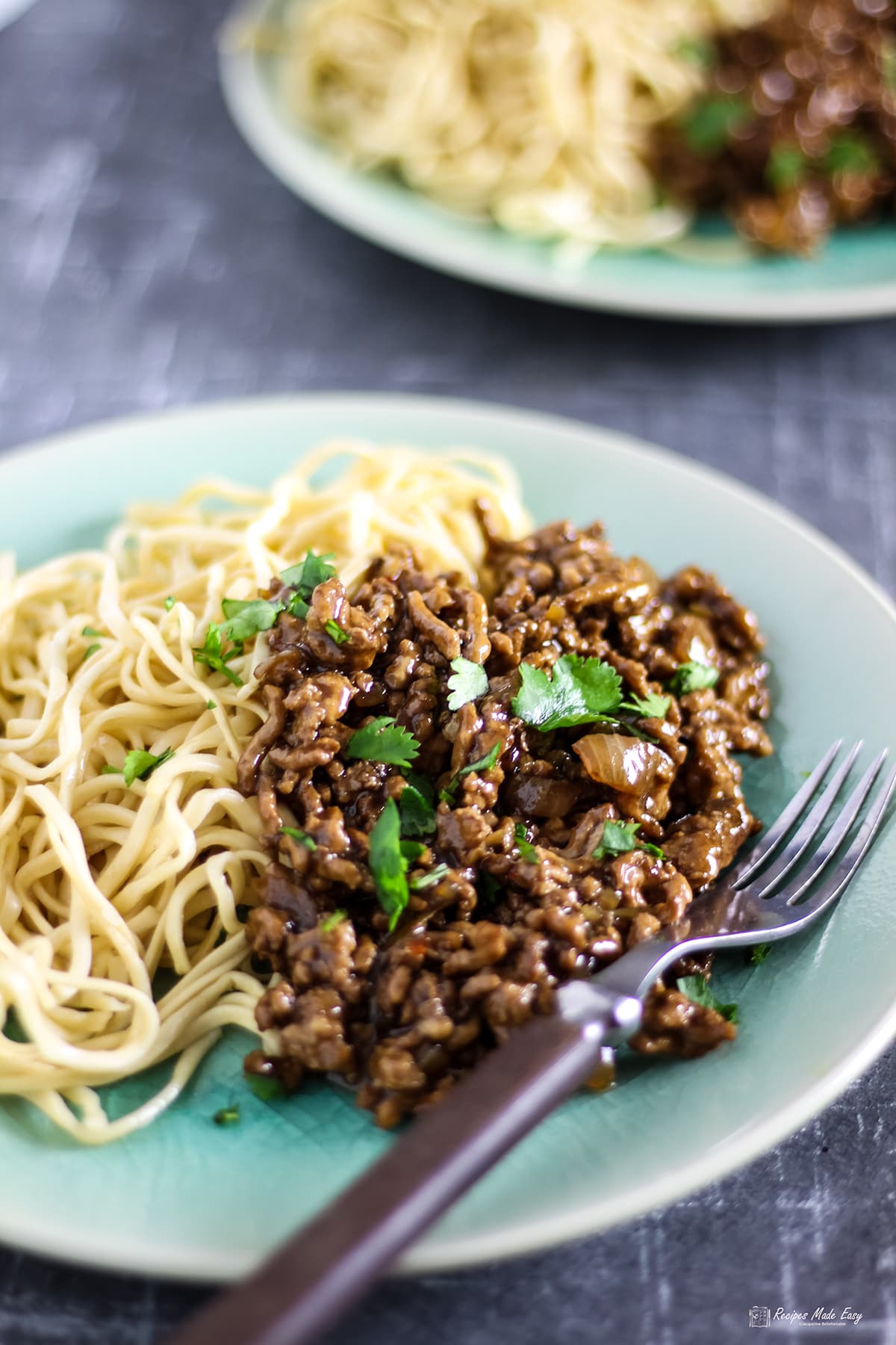 asian inspired spicy pork mince served with noodles on a green plate with fork on the side.