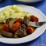 serving of old fashioned beef stew and carrots with mash potato. PIece of meat on fork on the side.