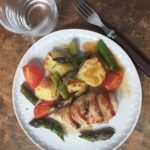 serving of chicken and asparagus traybake on plate with water glass and fork
