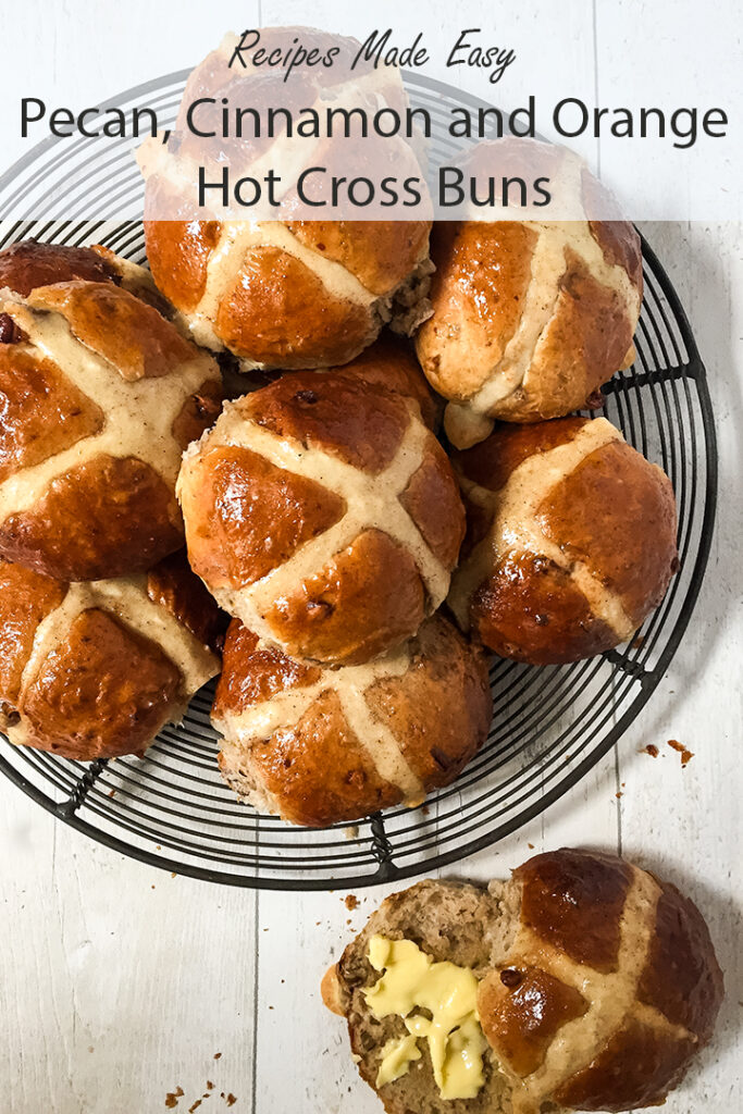 pecan cinnamon and orange hot cross buns on a wire rack with one cut open and buttered.