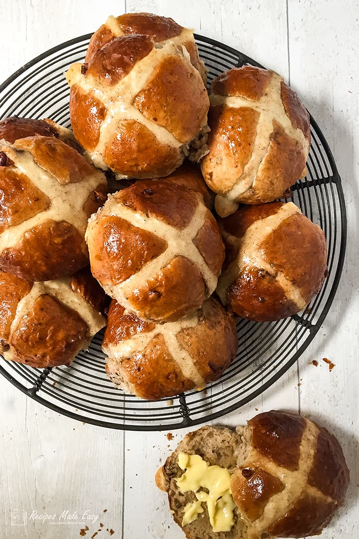 pecan cinnamon and orange hot cross buns on a wire rack with one cut open and buttered.