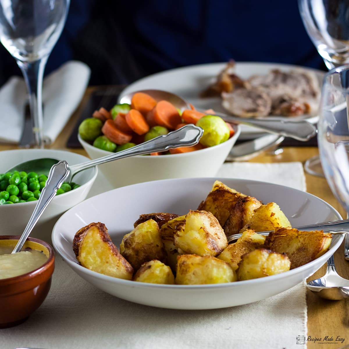 bowl of roast potatoes on a table with other veg behuind.