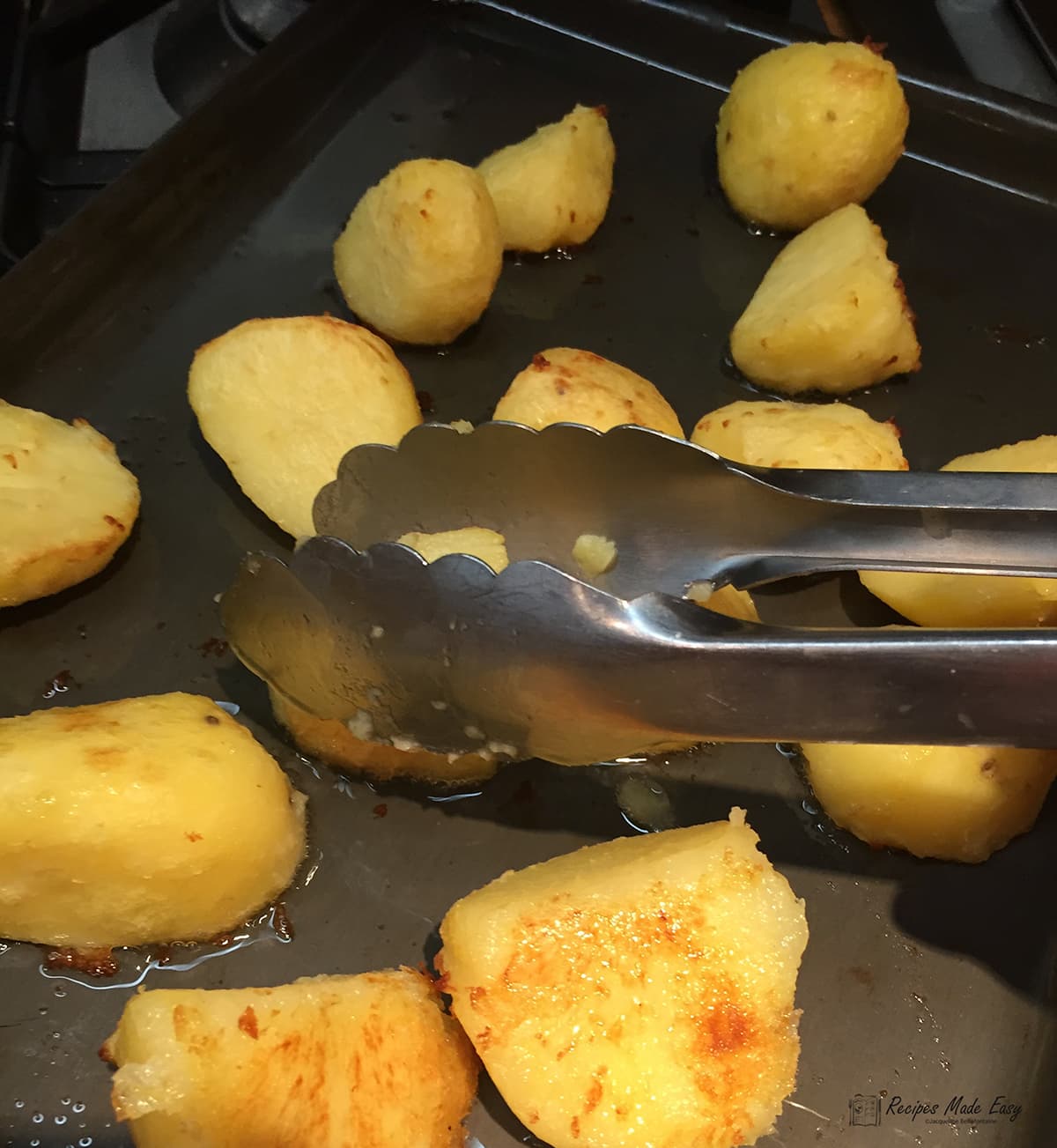 par boiled potatoes on tray being turned in the fat with tongs.