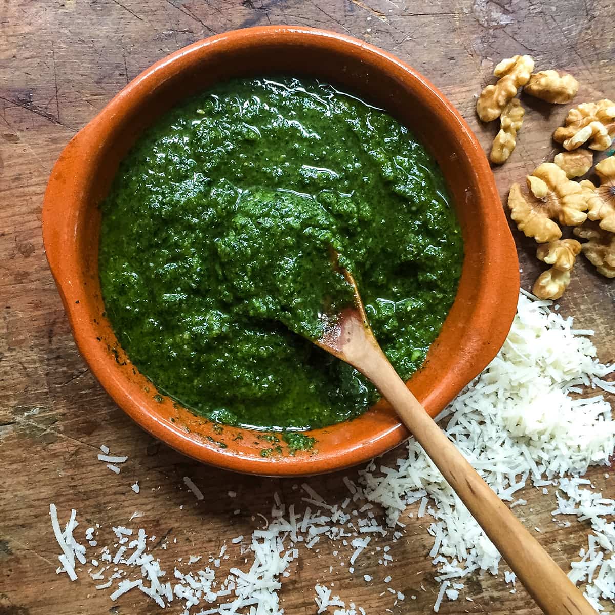 bowl of carrot top pesto with cheese and nuts around it.