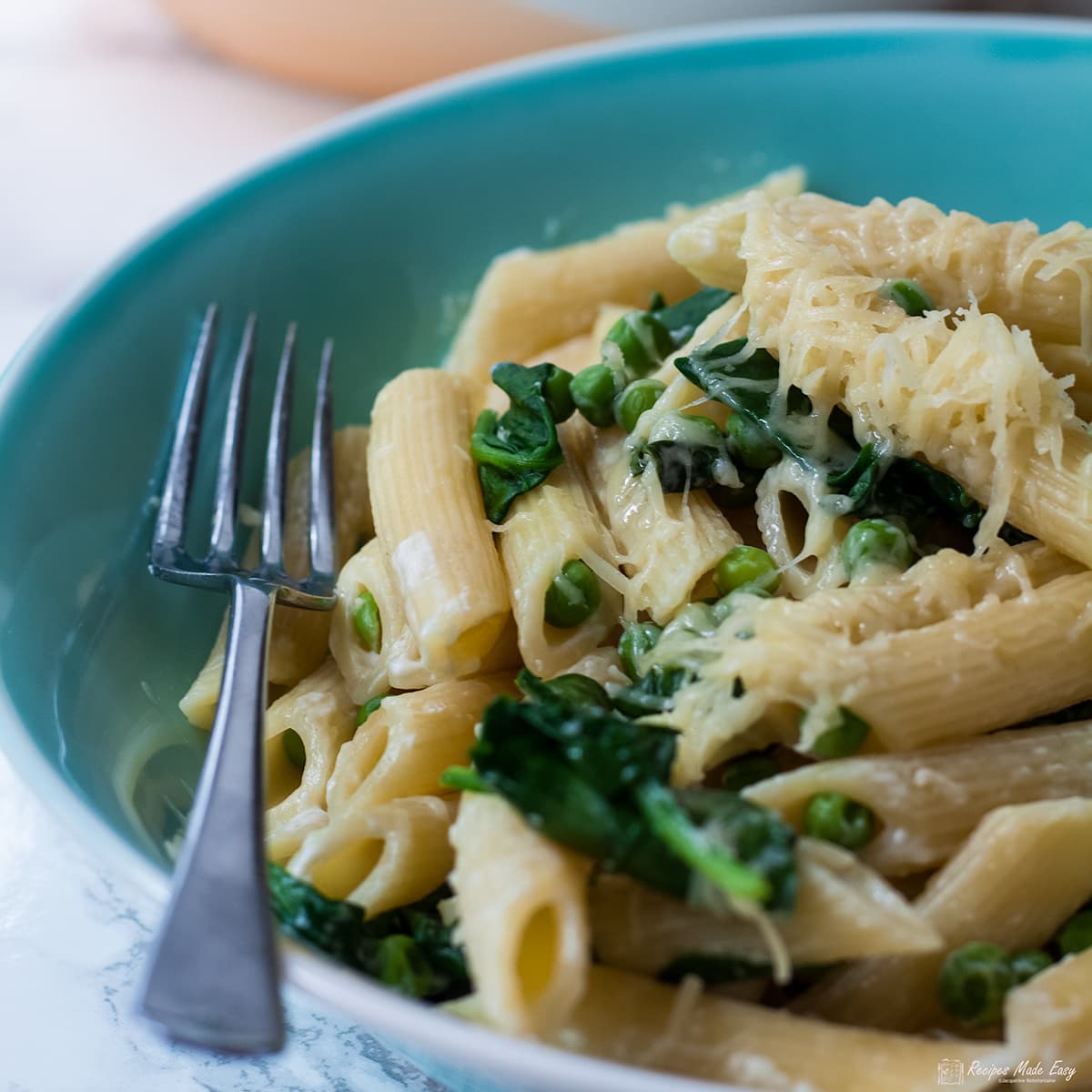 bowl of penne with spinach and peas with fork on the side.