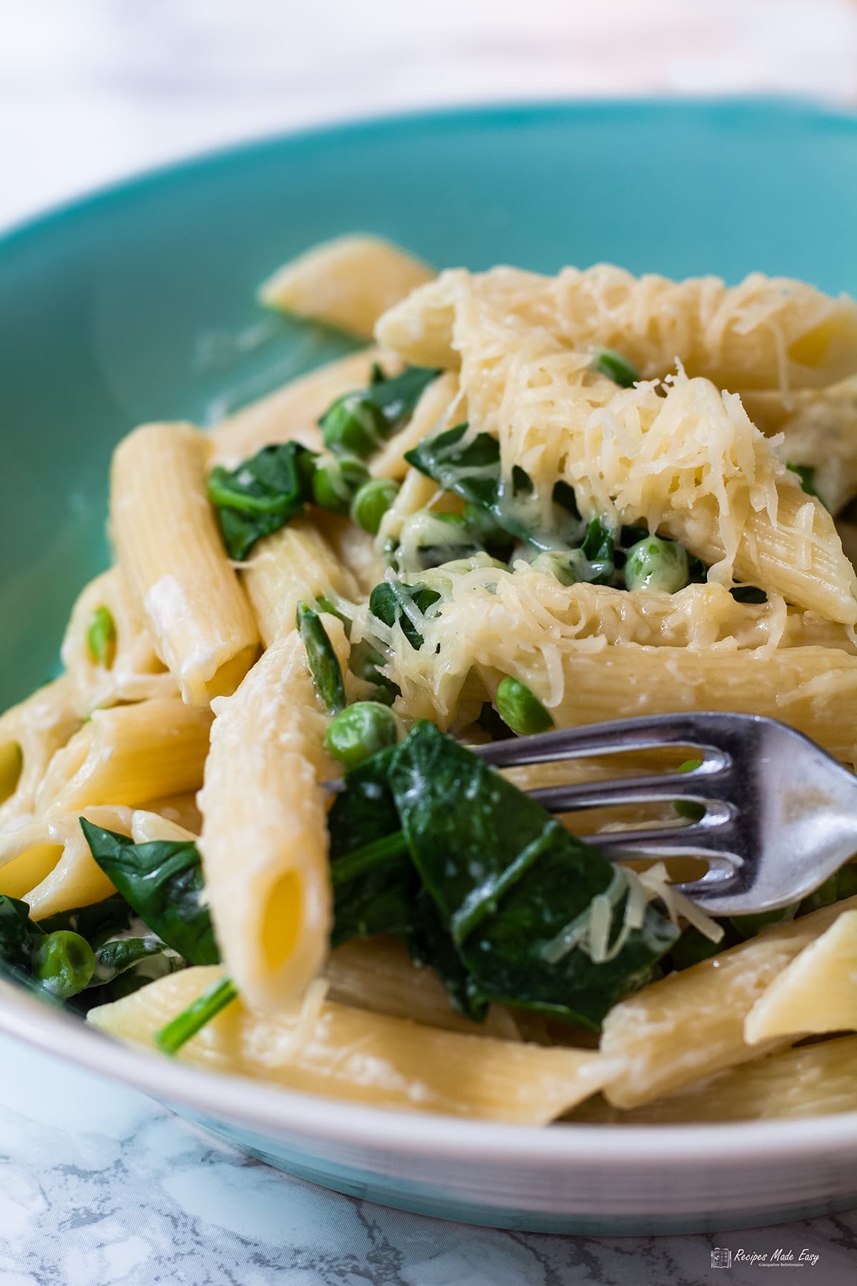 bowl of penne with spinach and peas with fork picking up some spinach.