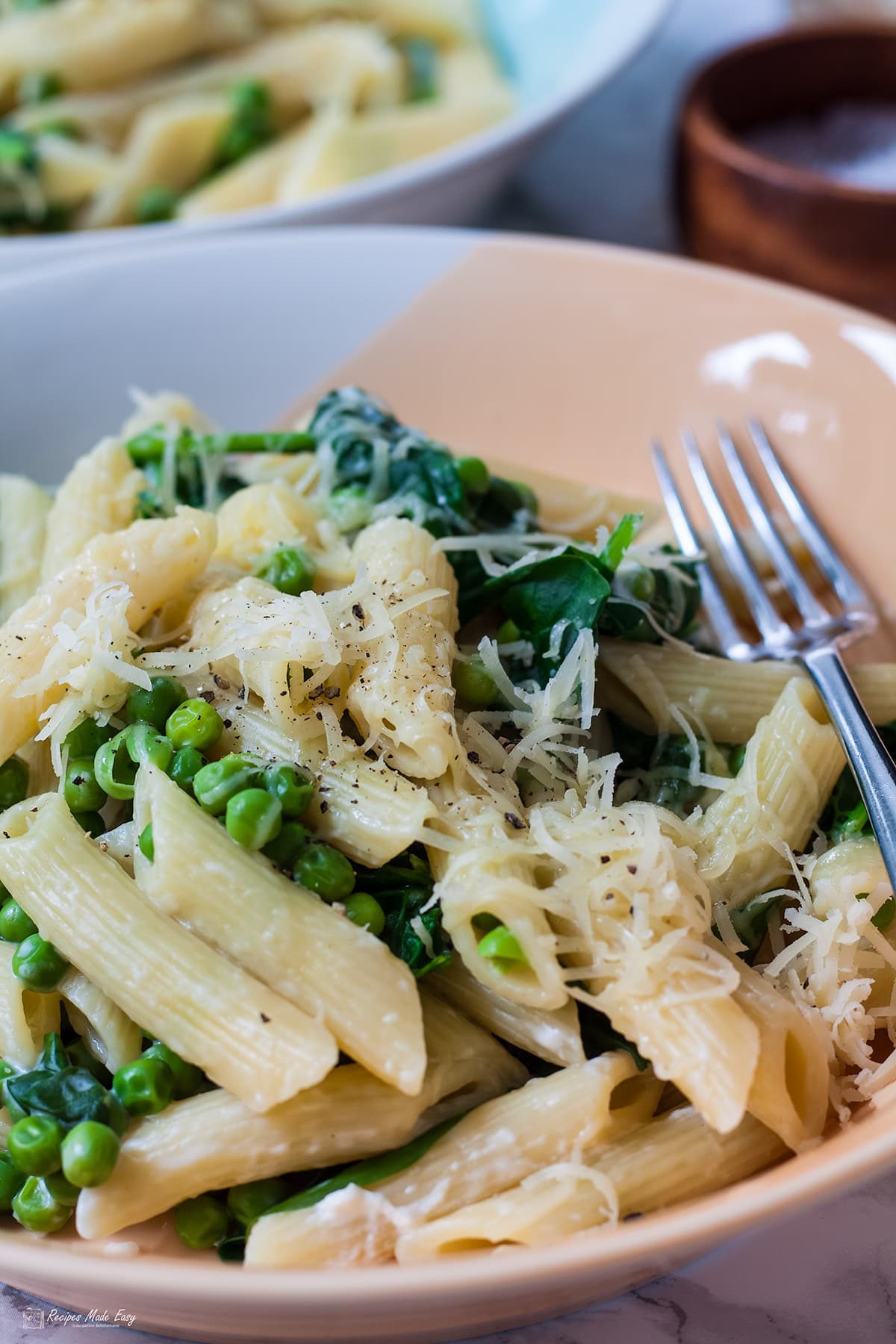 penne with spinach and peas in bowl with fork on side.
