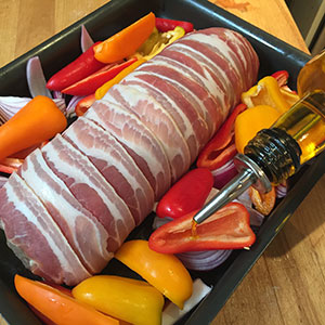 Drizzle the peppers and onion wedges with oil. uncooked joint in tin with peppers around being drizzled with oil