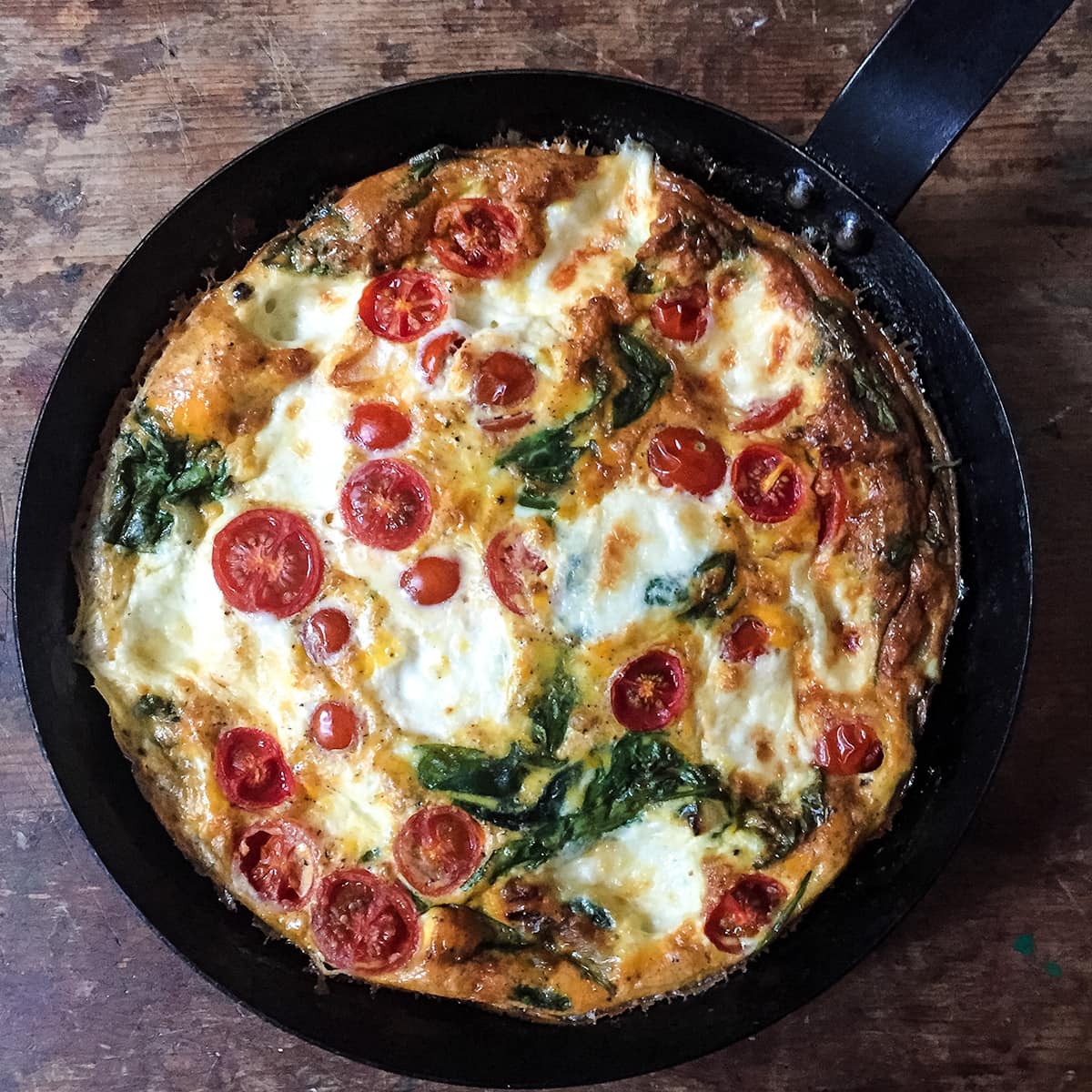 baked tomato spinach and mozzarella tortilla in a frying pan.