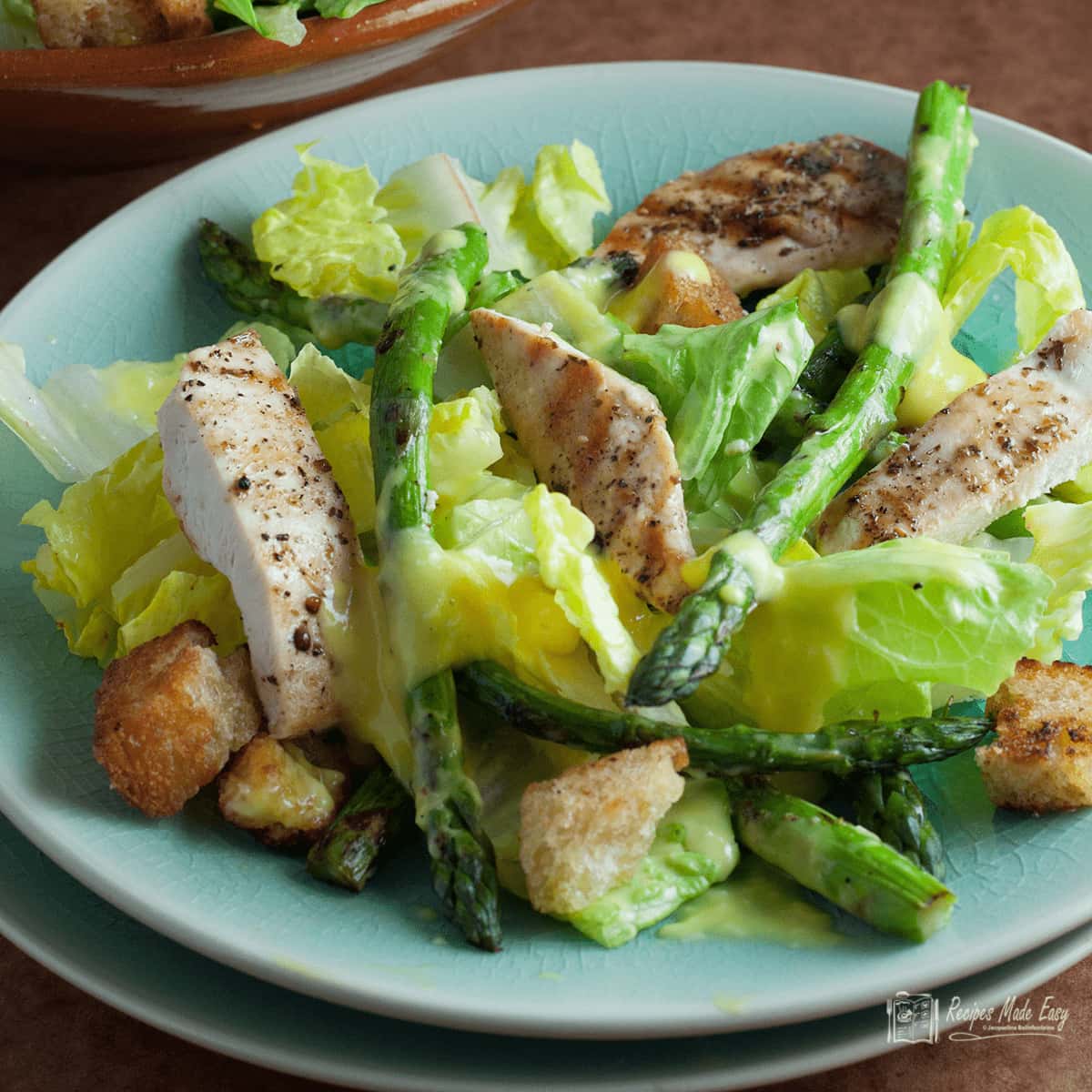 chicken and asparagus caesar salad on light blue plate.