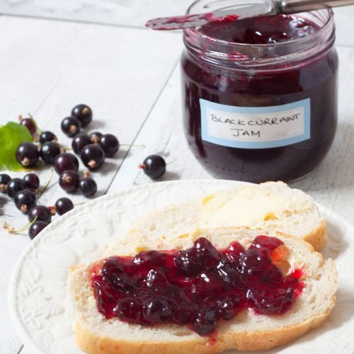 blackcurrant jam spread on bread with jar in background