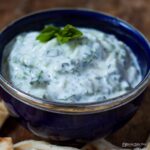 bowl of Tzatziki garnished with a small sprig of mint.