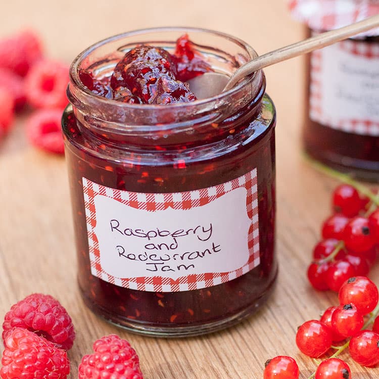 jar of raspberry and redcurrent jam with fruit around it.
