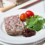 slice of ham hock terrine on plate with chutney and salad garnish