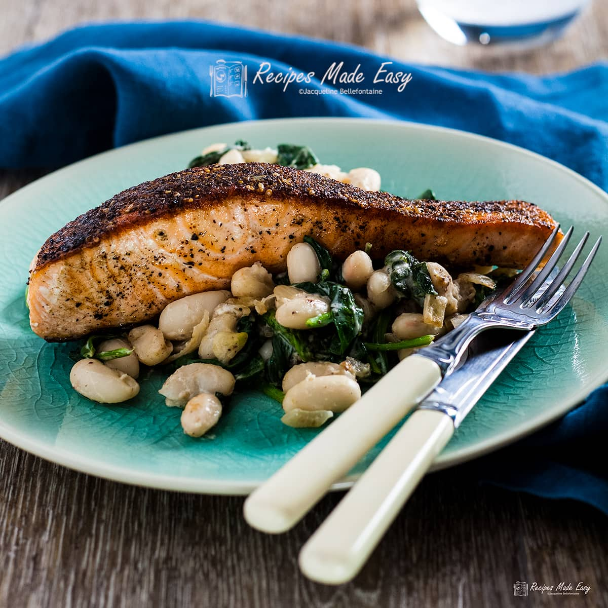 pan seared salmon with spinach and beans on a dinner plate with knife and fork.