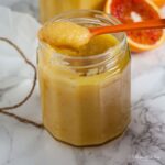 open jar of blood orange posset with spoon on top.