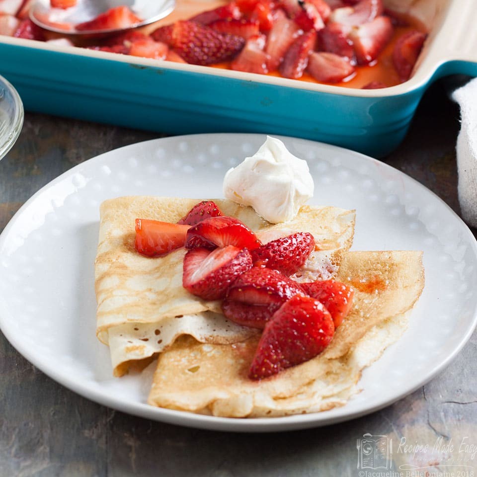 plate of pancakes topped with strawberries with dish in background