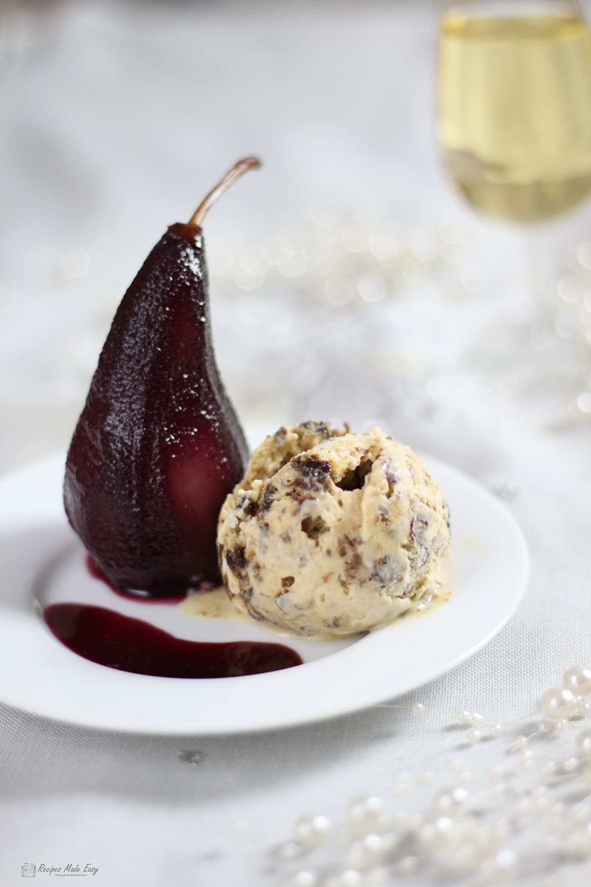 Pear poached in red wine served with Christmas pudding icecream with glass of fizzy wine behind.