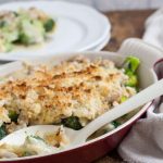 Chicken and broccoli au gratin in dish with serving spoon. plates in background