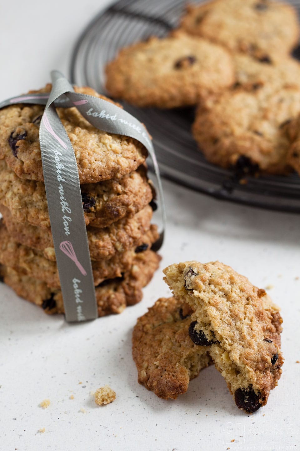 Oat and raisin cookies stacked into a bundle with some on plate behind and one broken open
