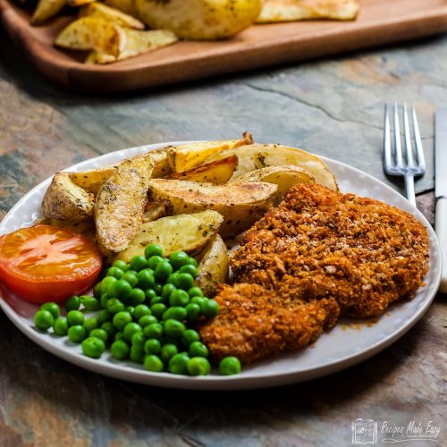 oven baked pork schnitzel served with chips peas and tomato