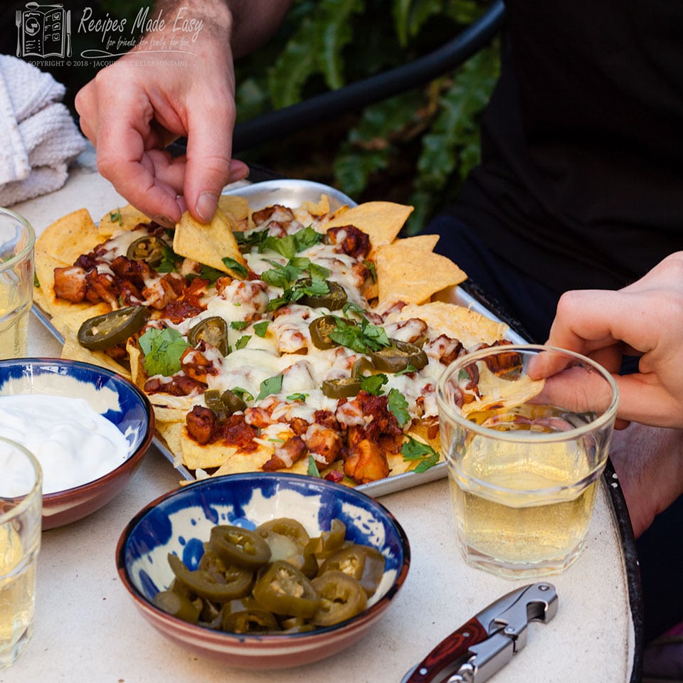 easy chicken nachos on a tray on the table, with hands picking up the tortilla chips