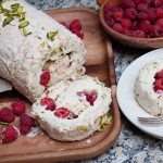 pistachio, raspberry and lemon meringue roll on wooden board with slice laying flat