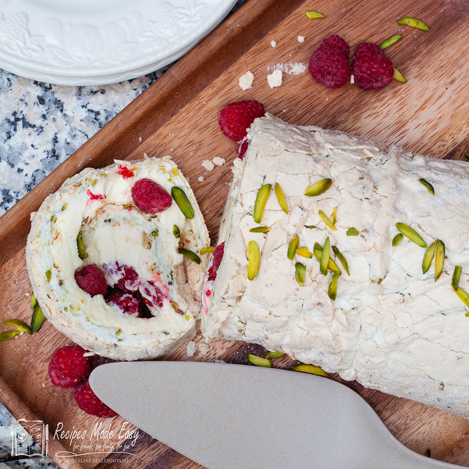 overhead shot of pistachio, raspberry and lemon meringue roll on a board with slice lying down