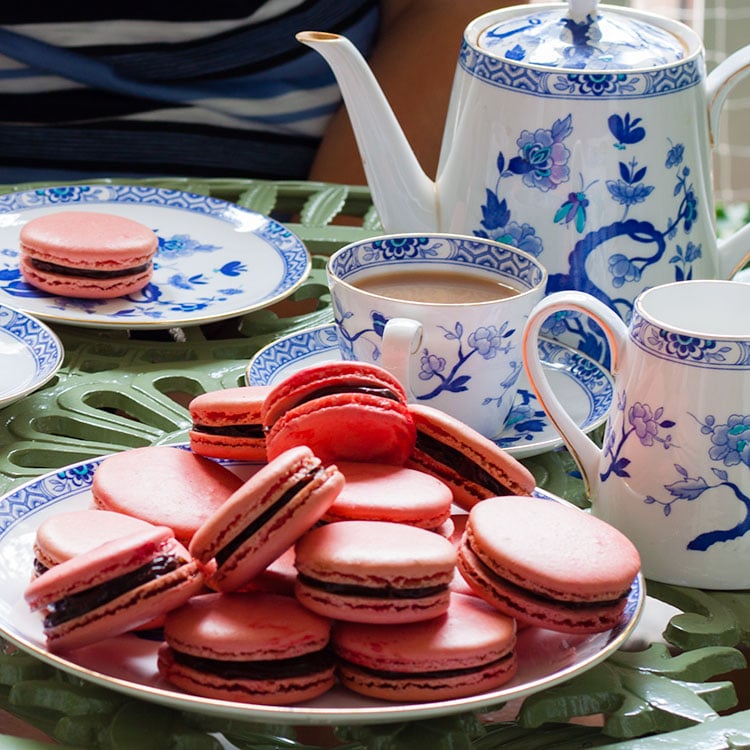 Macarons on a serving plate with tea set behind