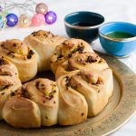 Chive and tomato bread ona serving plate with sipping bowl behind