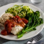 oven baked cod with chunky tomato sauce served on a plate with courgette and broccoli